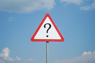 Warning road sign with question mark on a background of blue sky with clouds.