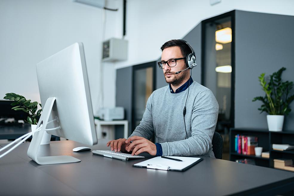 Young male customer support with headset working on the computer. ヘッドセットを装着した若い男性ITスペシャリストが、コンピュータでインフラ分析に取り組んでいます。